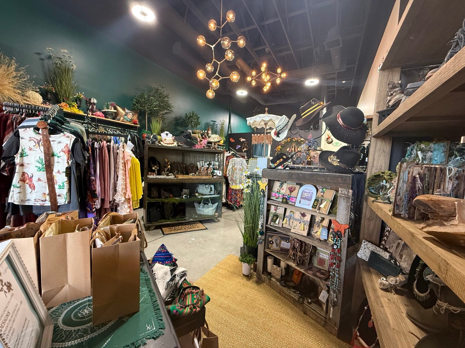 Inside Aurum Grove: racks of clothing, hats and decor under gold chandeliers